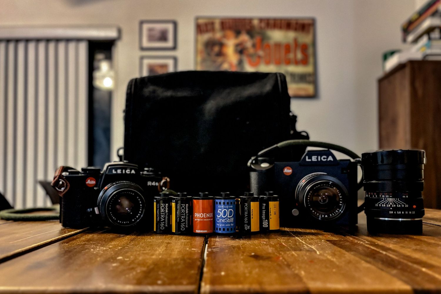 Vintage film cameras and rolls displayed on wooden table with black camera bag.