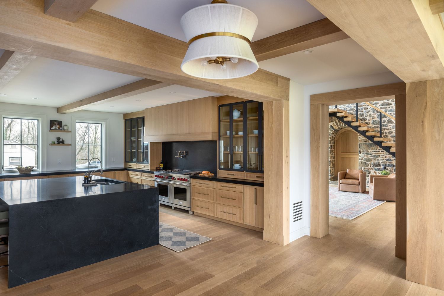 Modern kitchen with wood beam ceiling, black island, built-in cabinetry, hardwood floors, and open archway to living area.
