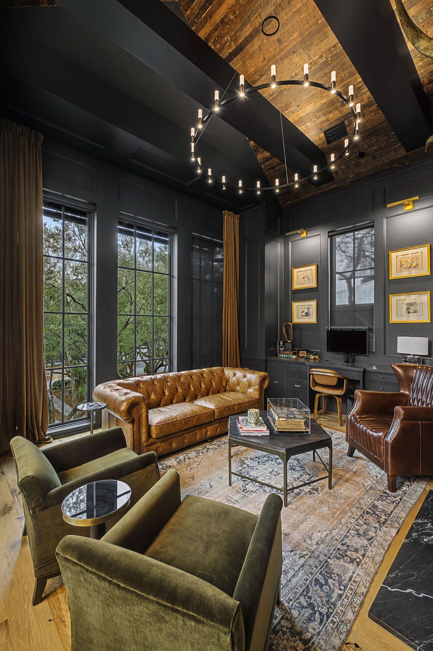 Elegant dark-walled living room with tufted leather sofa, velvet chairs, wood ceiling, and circular chandelier.