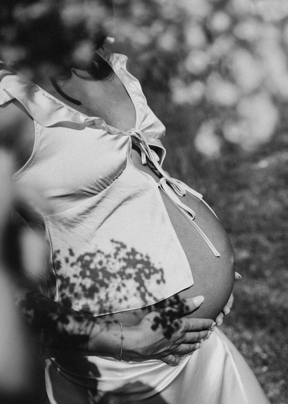 Black and white maternity portrait showing pregnant belly in tied white top.