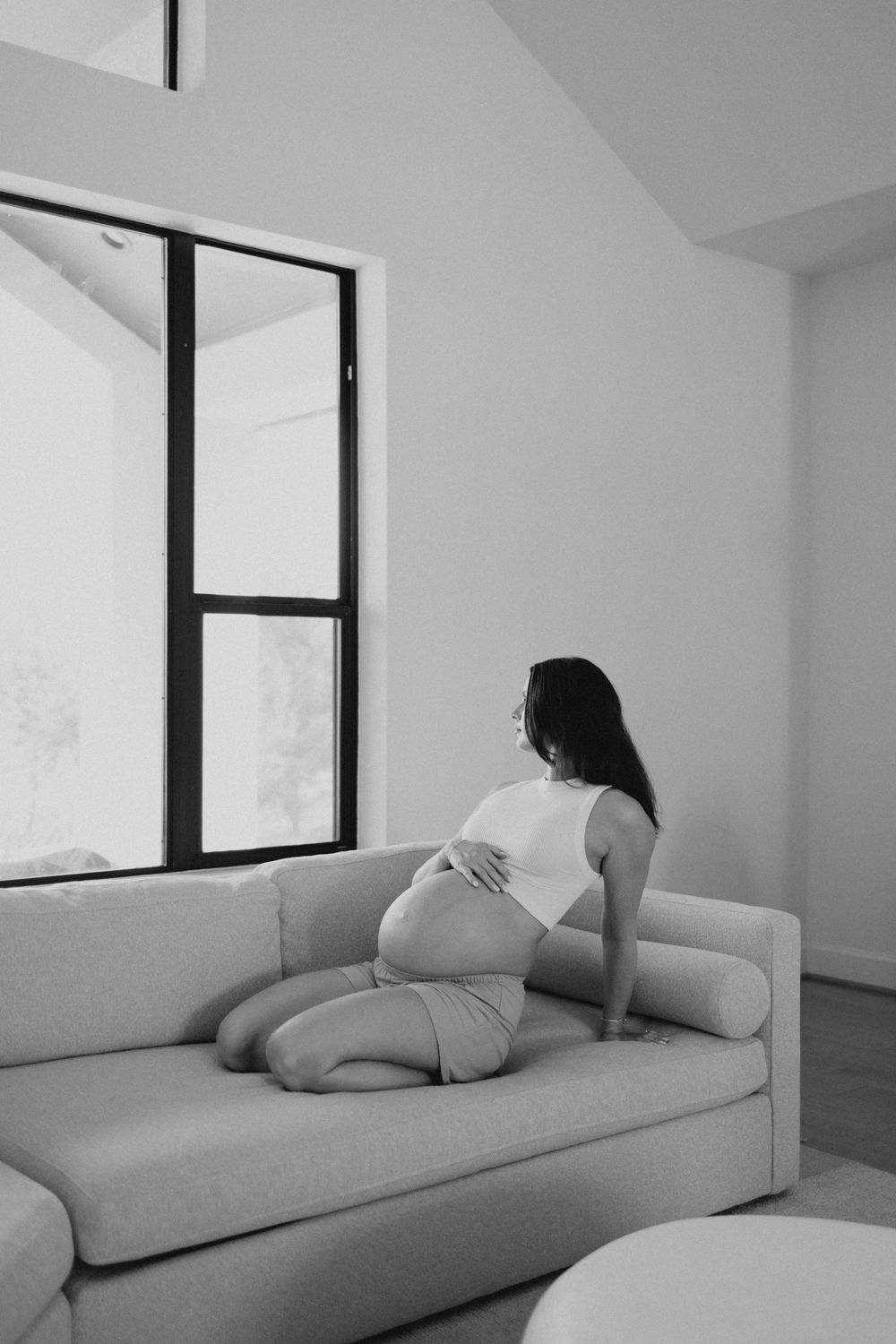 Black and white photos showing a person resting on a minimalist couch in a bright room.