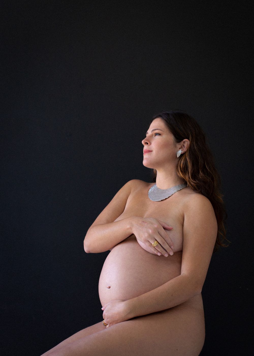 Elegant maternity portraits against dark backdrop highlighting the pregnant silhouette.