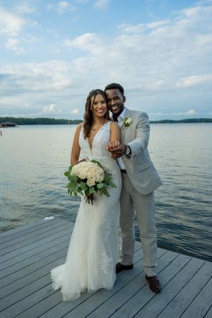 Bride and groom on dock with water in background showing rings