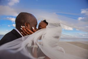 Bride and groom, kissing on beach with veil dramatically around them