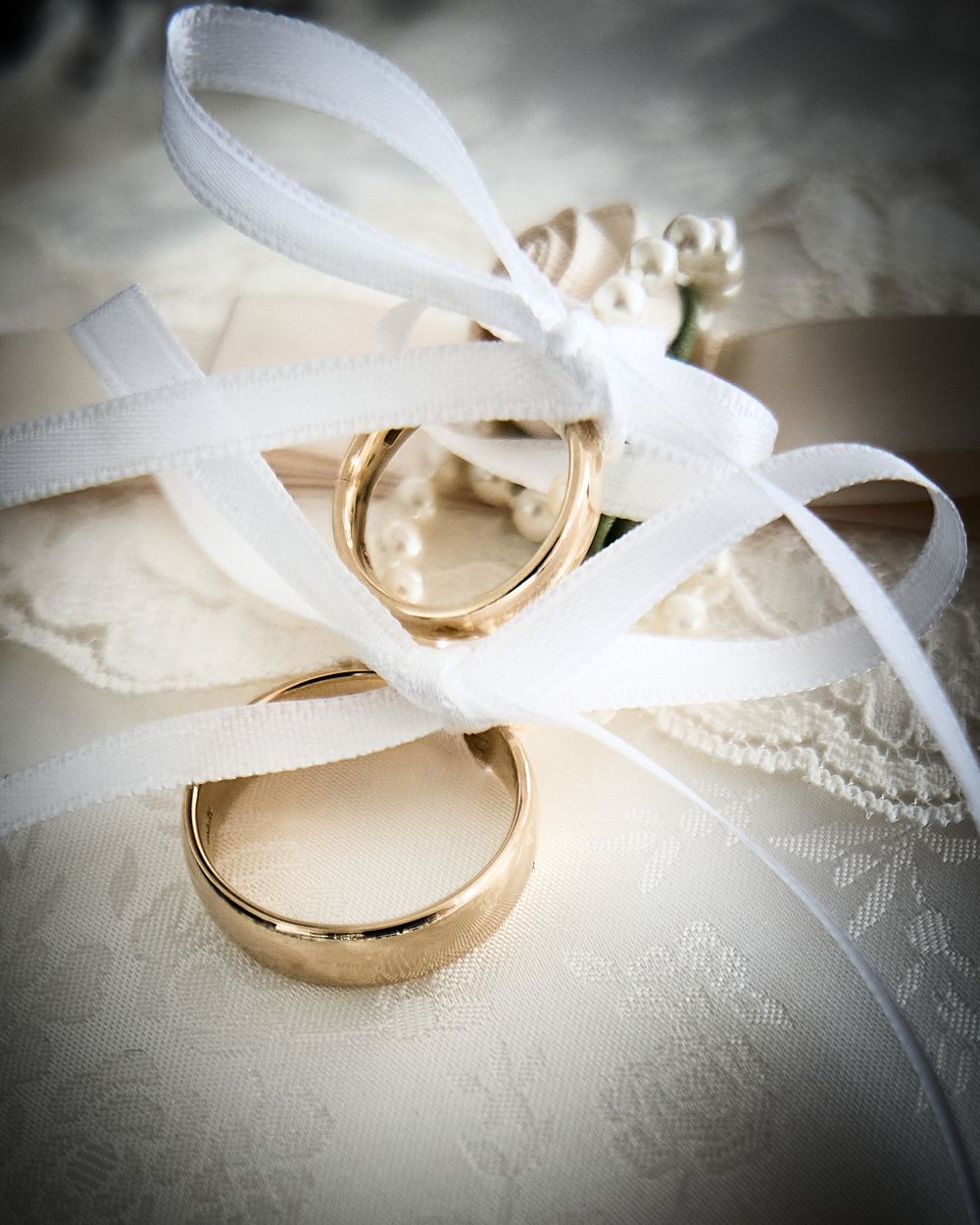 Two gold wedding rings tied with white ribbon on lace fabric in elegant wedding detail shot.