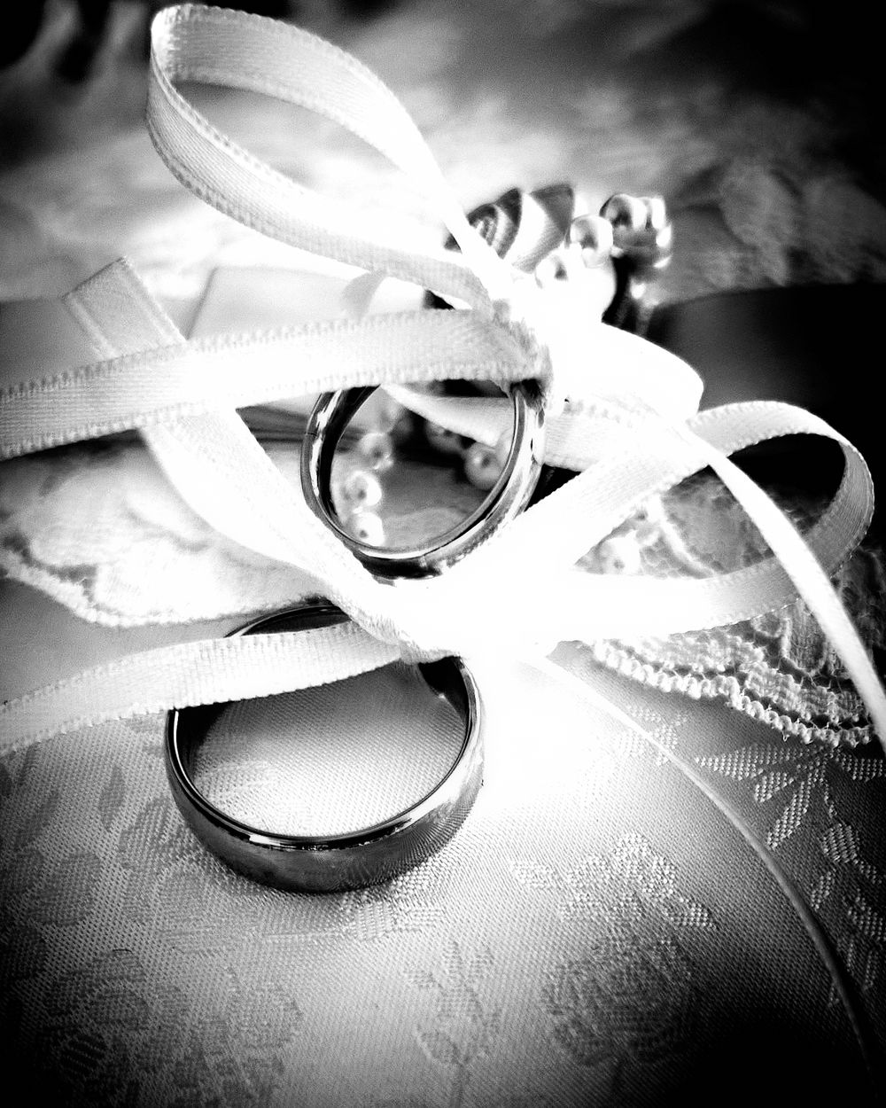 A black and white close-up of wedding rings with decorative white ribbon.