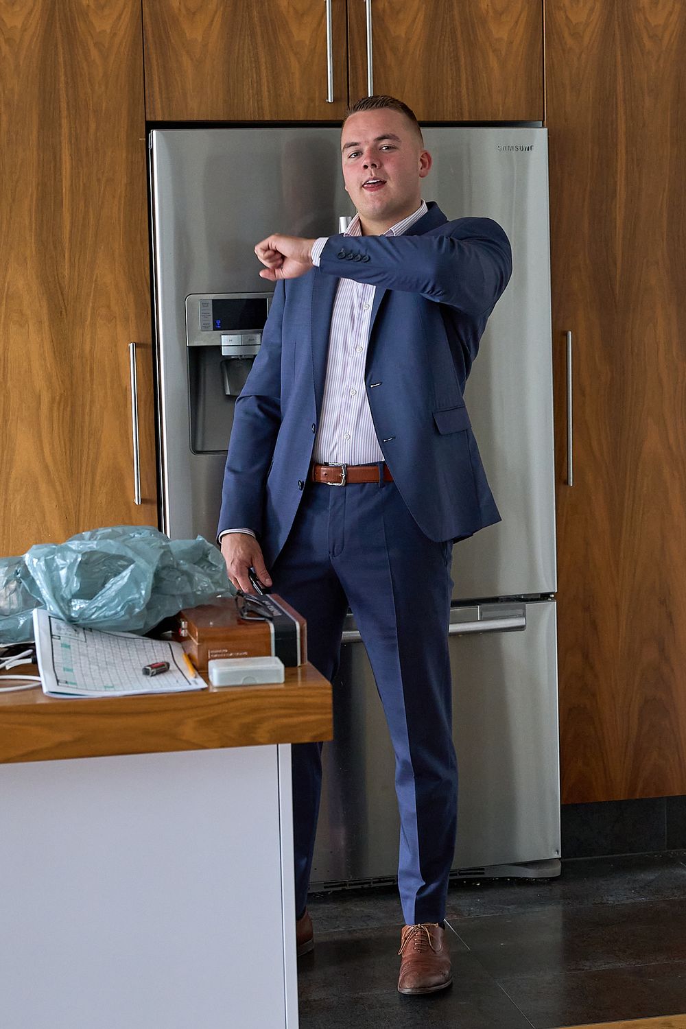 Person in navy suit checking time while standing in modern kitchen with wood paneling.