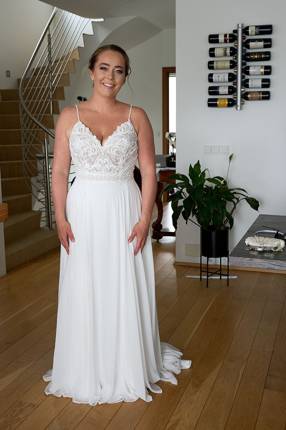 A wedding dress with lace bodice and flowing white skirt in modern home interior with wine rack display.