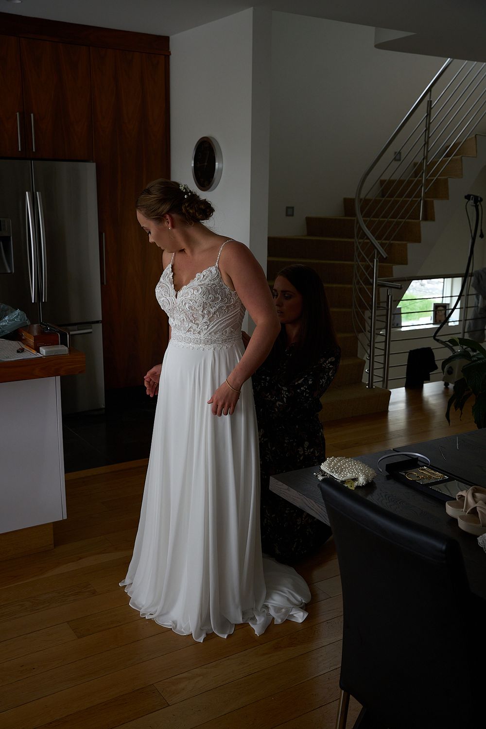 Wedding dress fitting in modern home interior with staircase and hardwood floors.