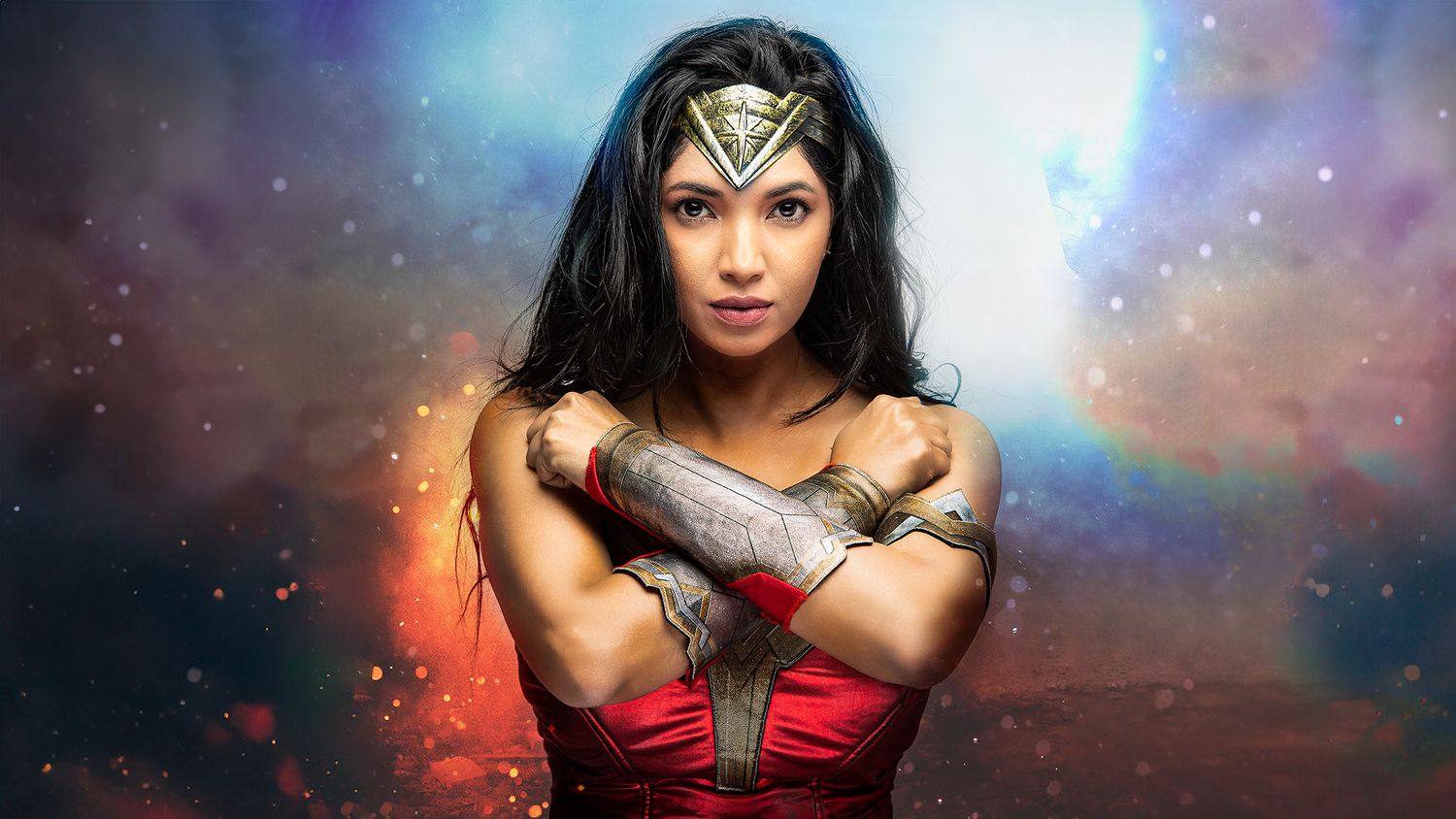 Superhero in red and gold armor costume stands with crossed arms against a colorful cosmic background.