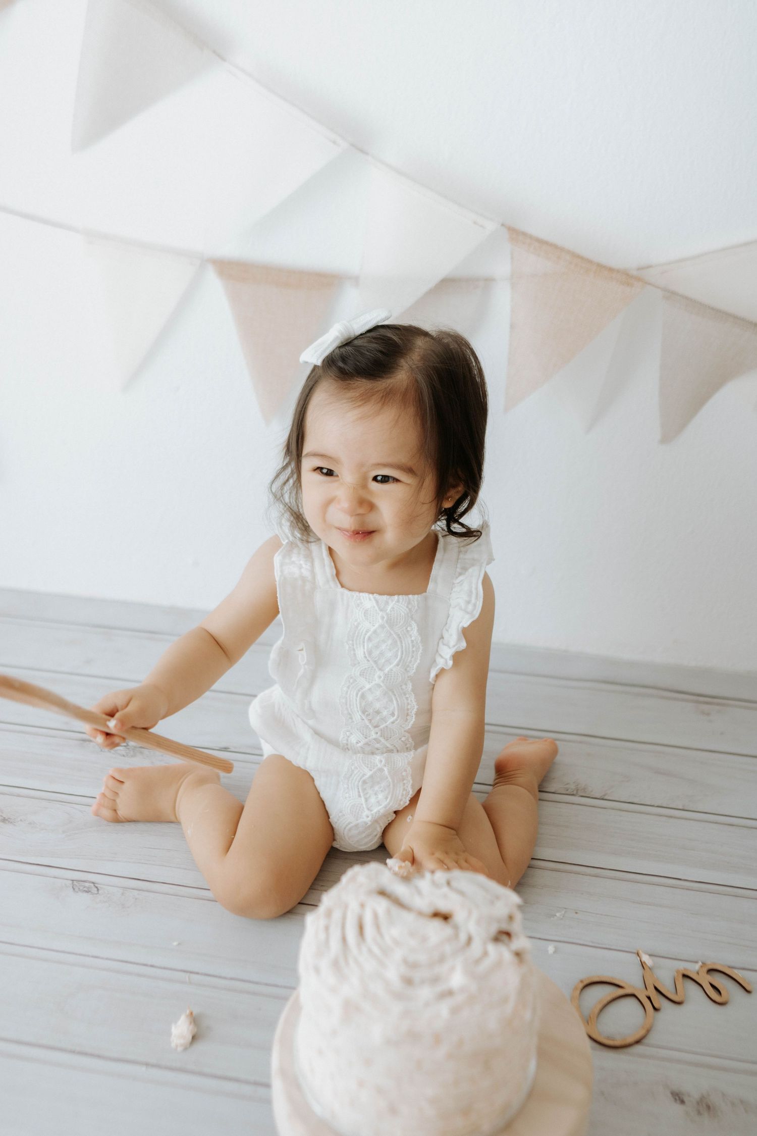White lace romper outfit with bunting flags and cake on wooden floor. cake smash in a natural light studio in the blue mountains Sydney