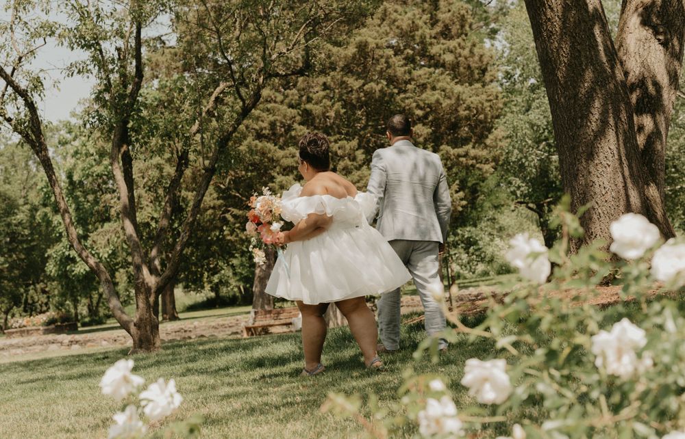 A couple walks through a garden surrounded by white flowers on a sunny spring day.