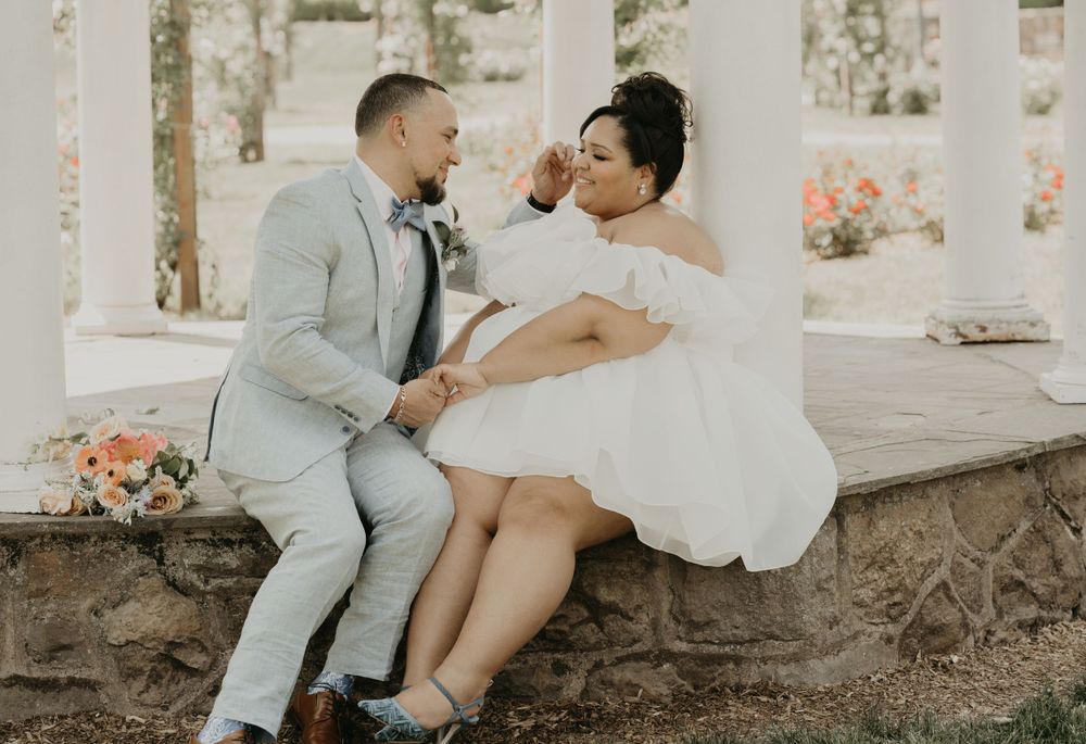 Wedding couple sharing a romantic moment on a stone wall under white columns.