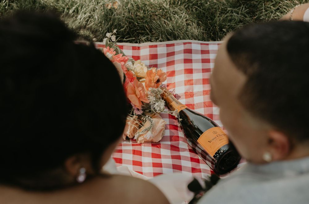 Couple popping champagne during their wedding picnic celebration.