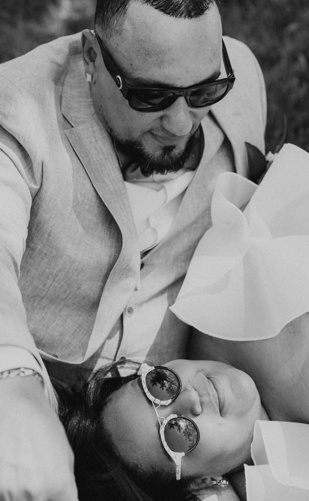 Black and white wedding portrait of couple in sunglasses lying together.