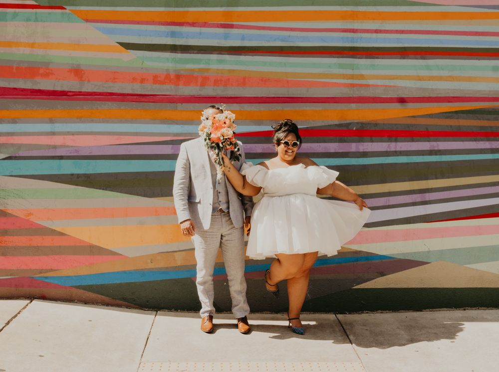 Couple in wedding attire posing together against a colorful striped mural.