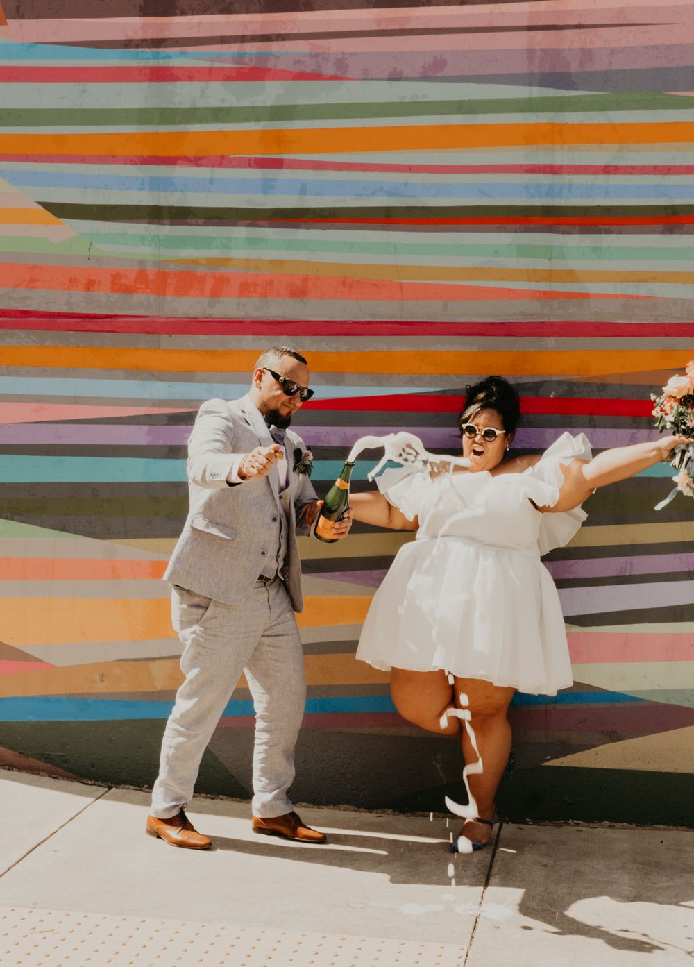 Wedding couple dancing joyfully against a colorful striped wall backdrop.