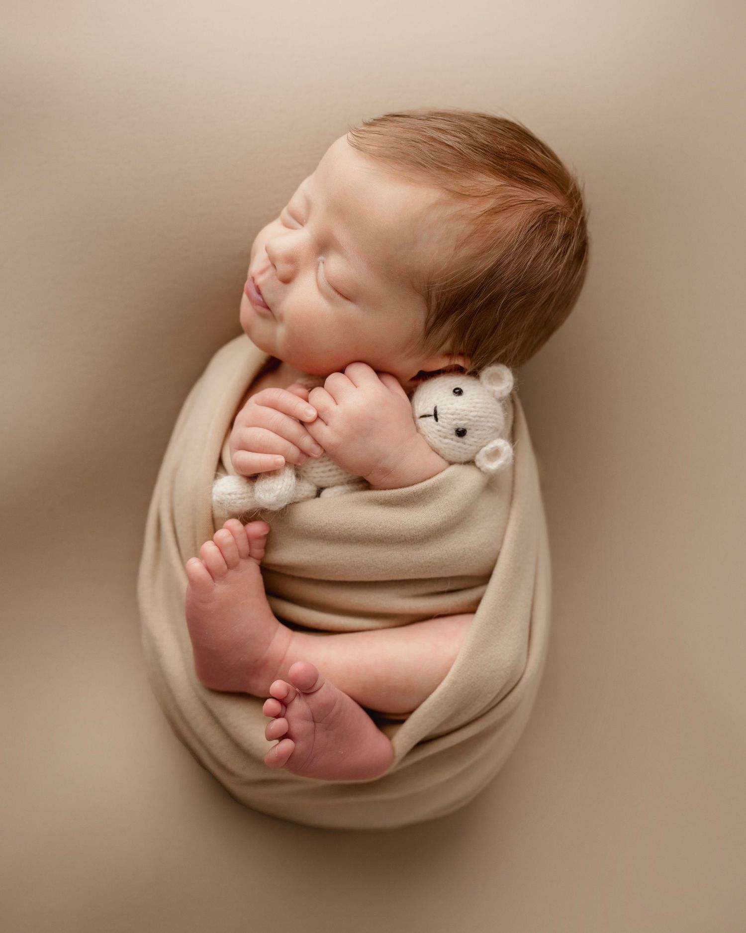 Artistic newborn portrait with baby wrapped in beige fabric holding small stuffed toy.  Middle TN Newborn Photographer.