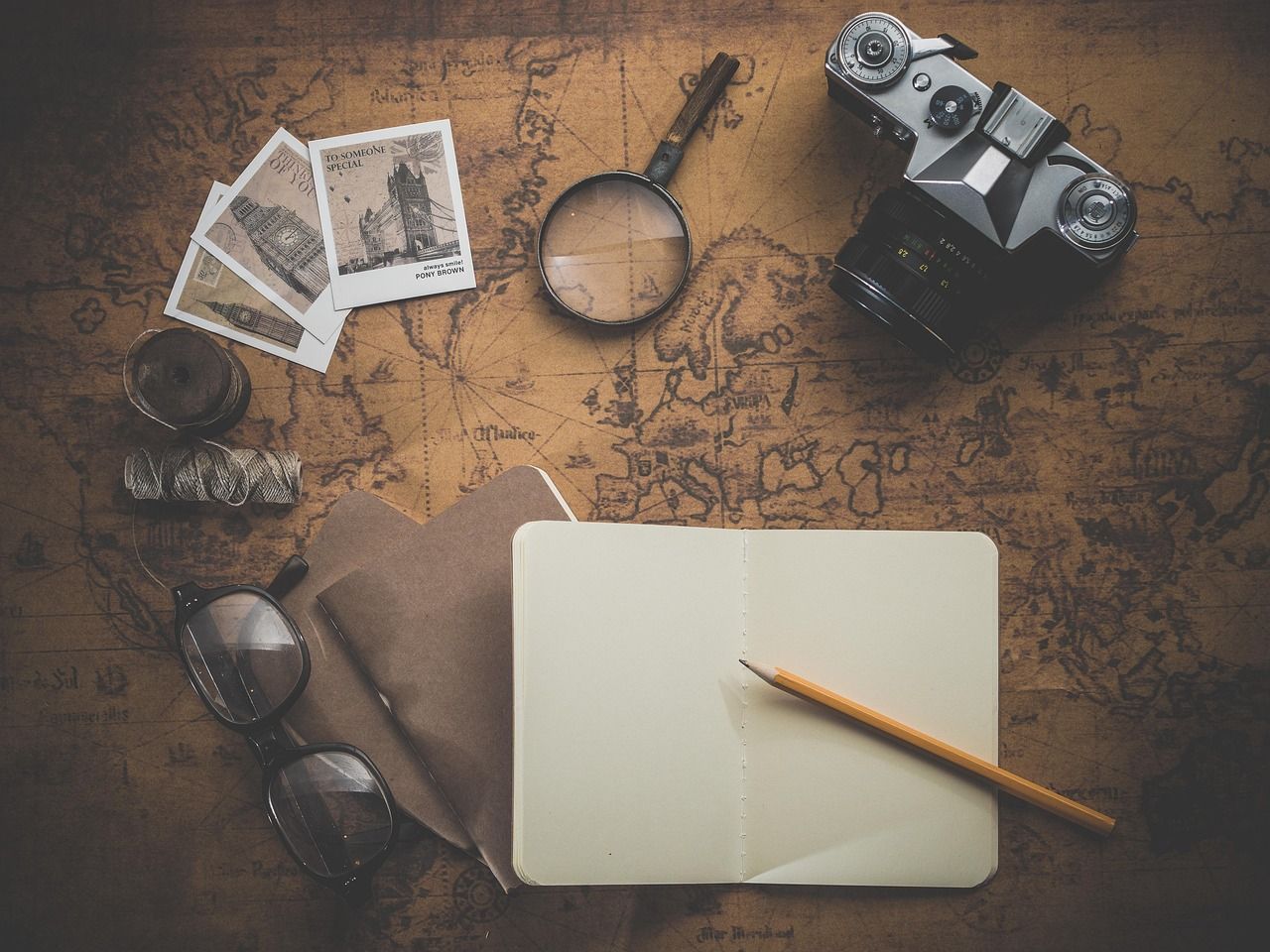 Vintage camera and blank paper with pencil on rustic wooden table with dramatic lighting and moody atmosphere.