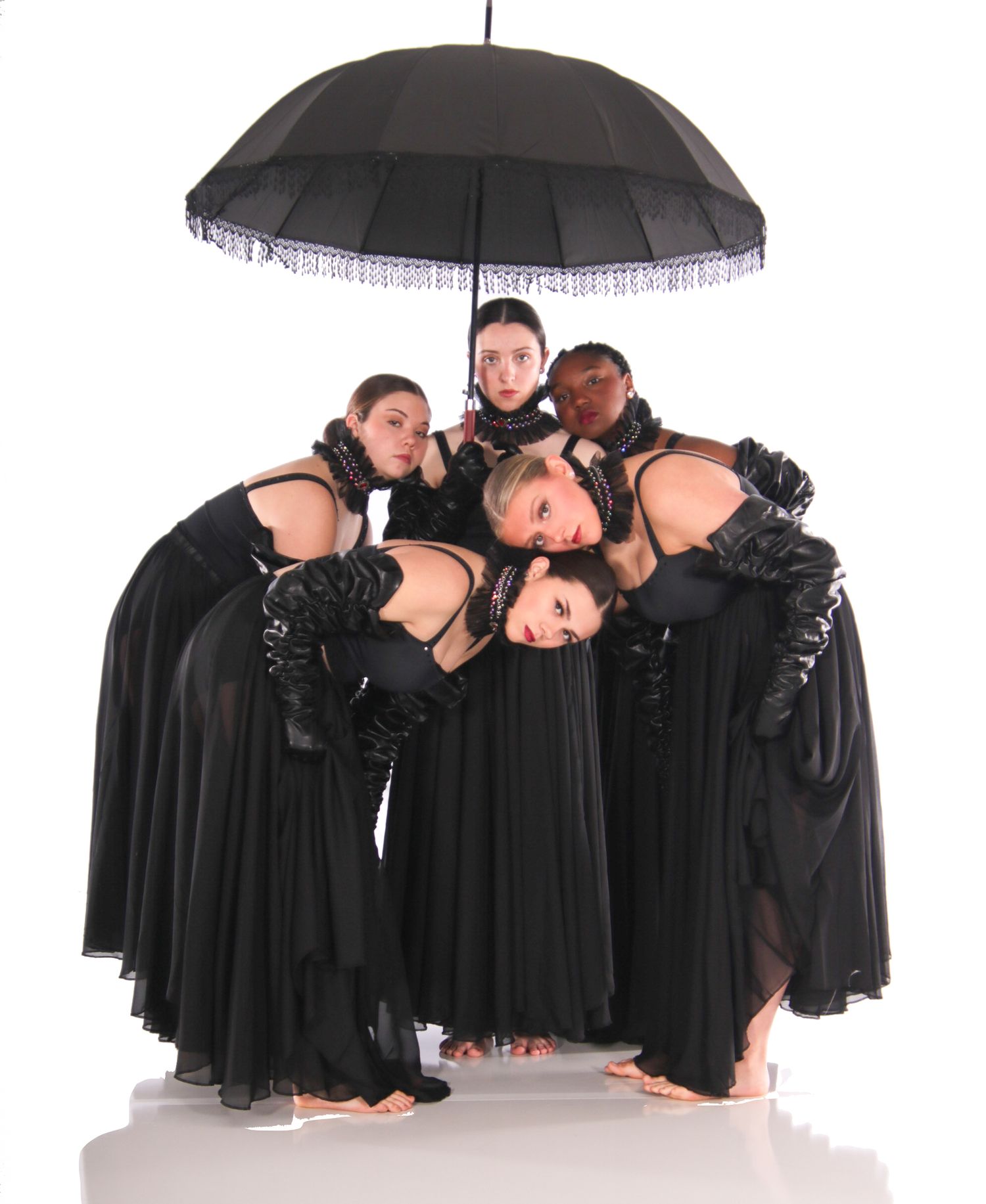 Dance group in black dresses posing with black umbrellas in artistic formation.
