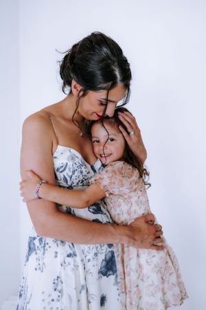 Two people in floral dresses share tender moments against a white backdrop in a series of intimate poses.