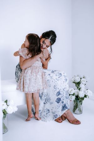 Two people in matching floral dresses sit close together against a white background with flowers.