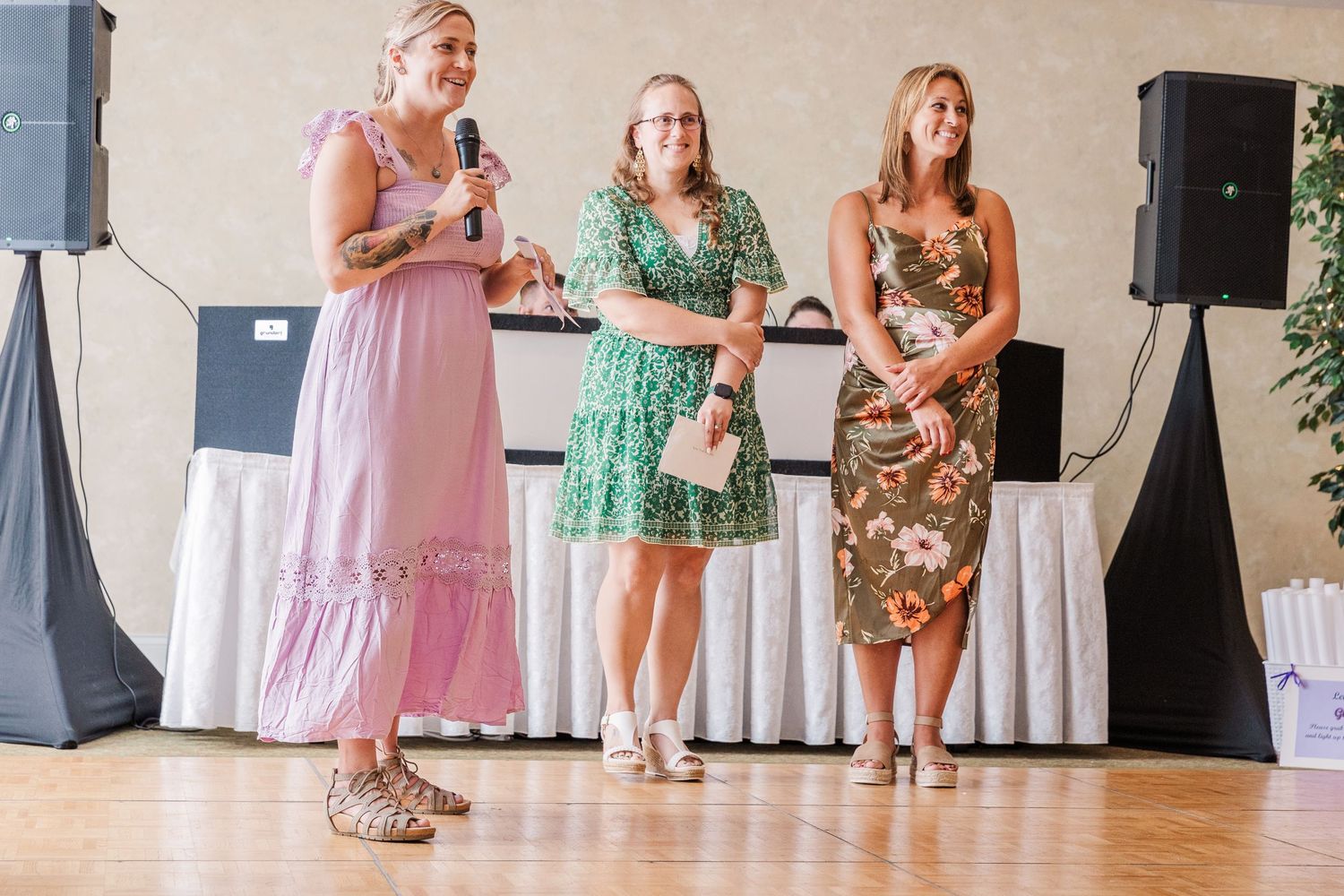 Three people speaking at a wedding reception with speakers and white draping in the background.