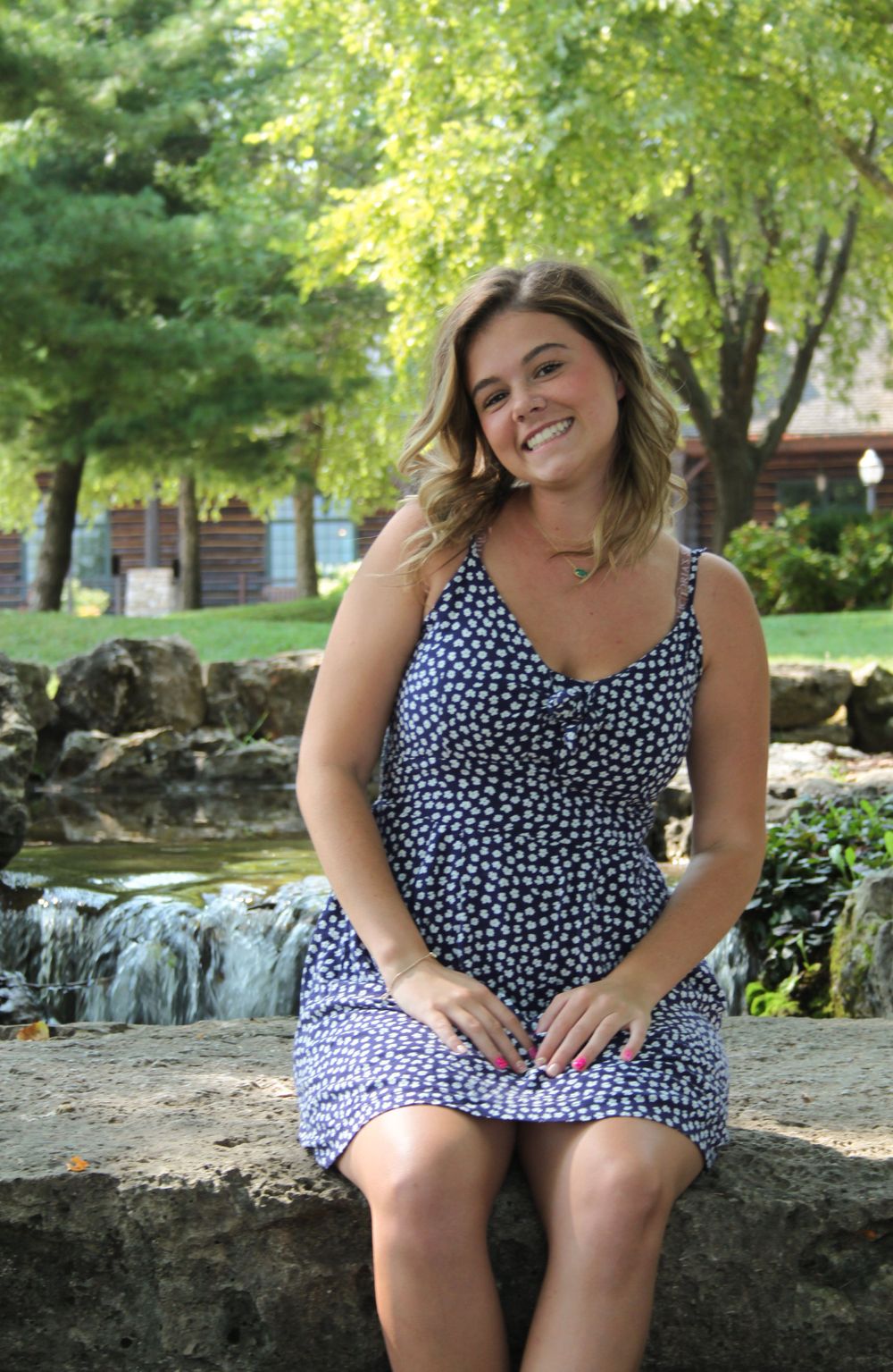 Girl smiling sitting on a waterfall at college of the ozarks in front of trees.