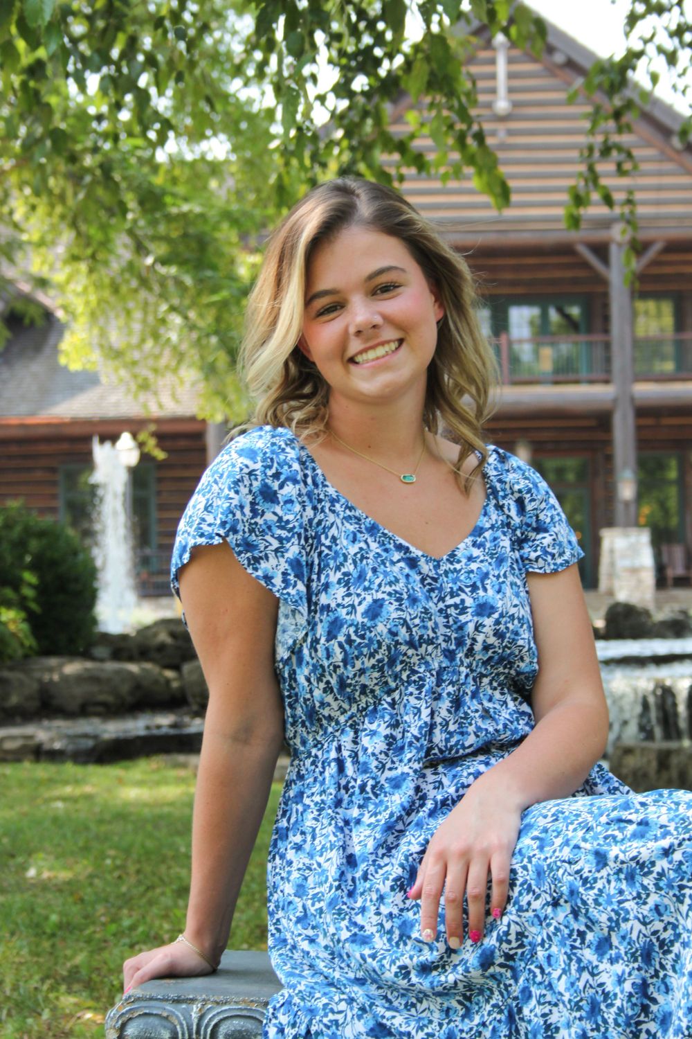 Girl smiling at College of the Ozarks in front of trees.