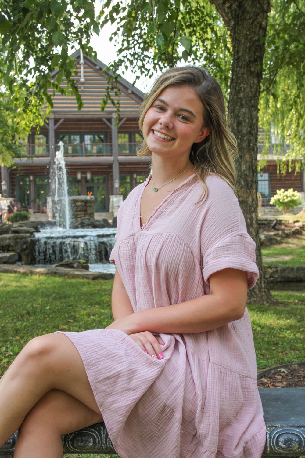 Girl smiling at College of the Ozarks in front of trees for senior pictures.