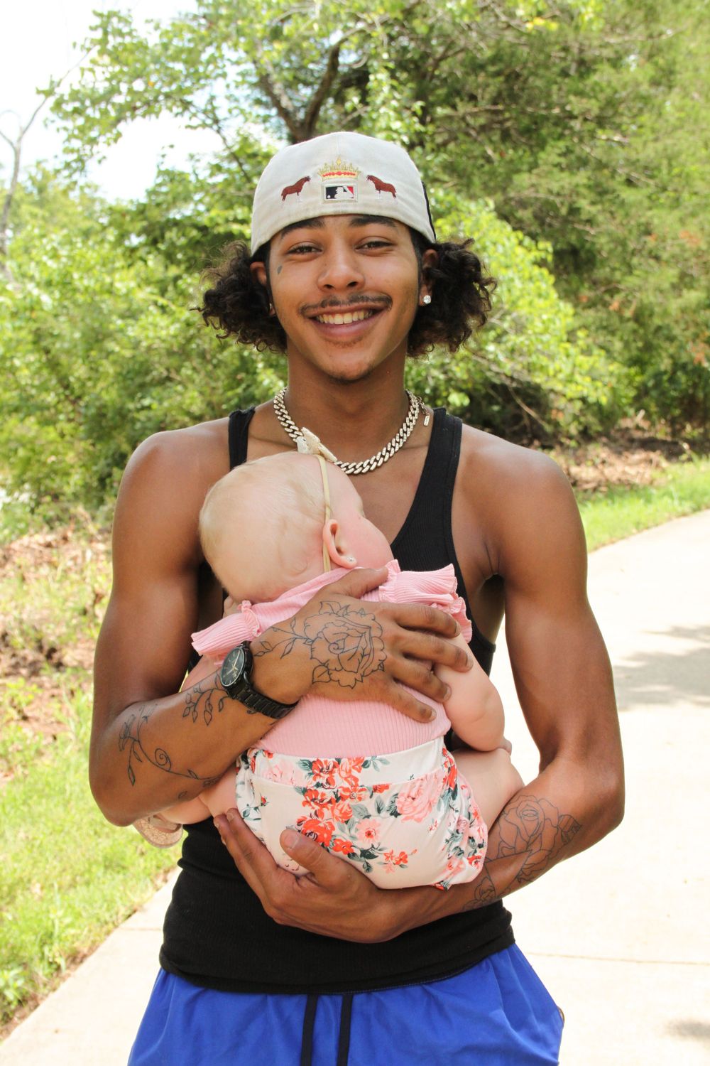 Man holding baby girl smiling at stockstill park in front of trees.