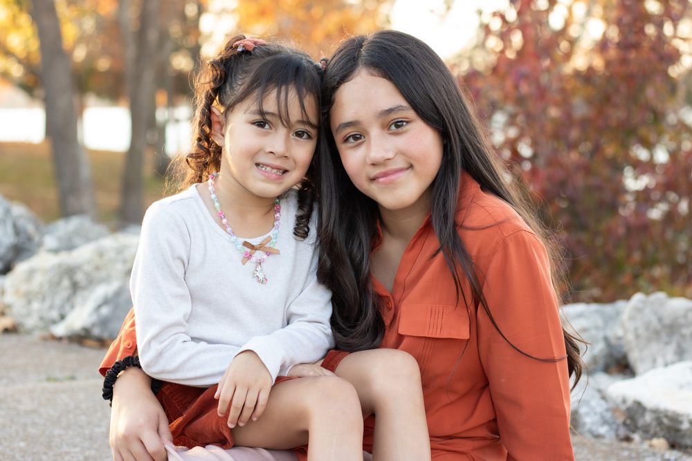 Two girls holding each other and smiling at the camera by the lake.