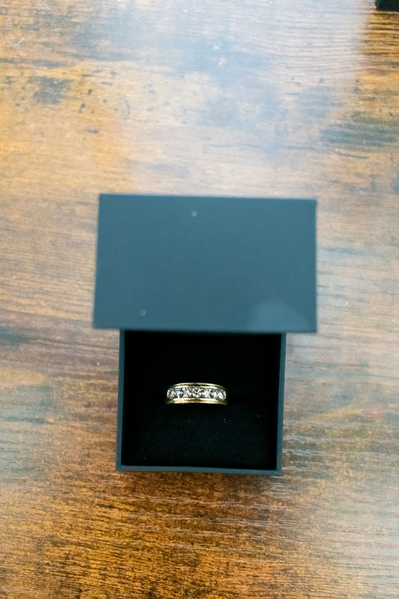 Diamond ring in black jewelry box sitting on wooden surface.