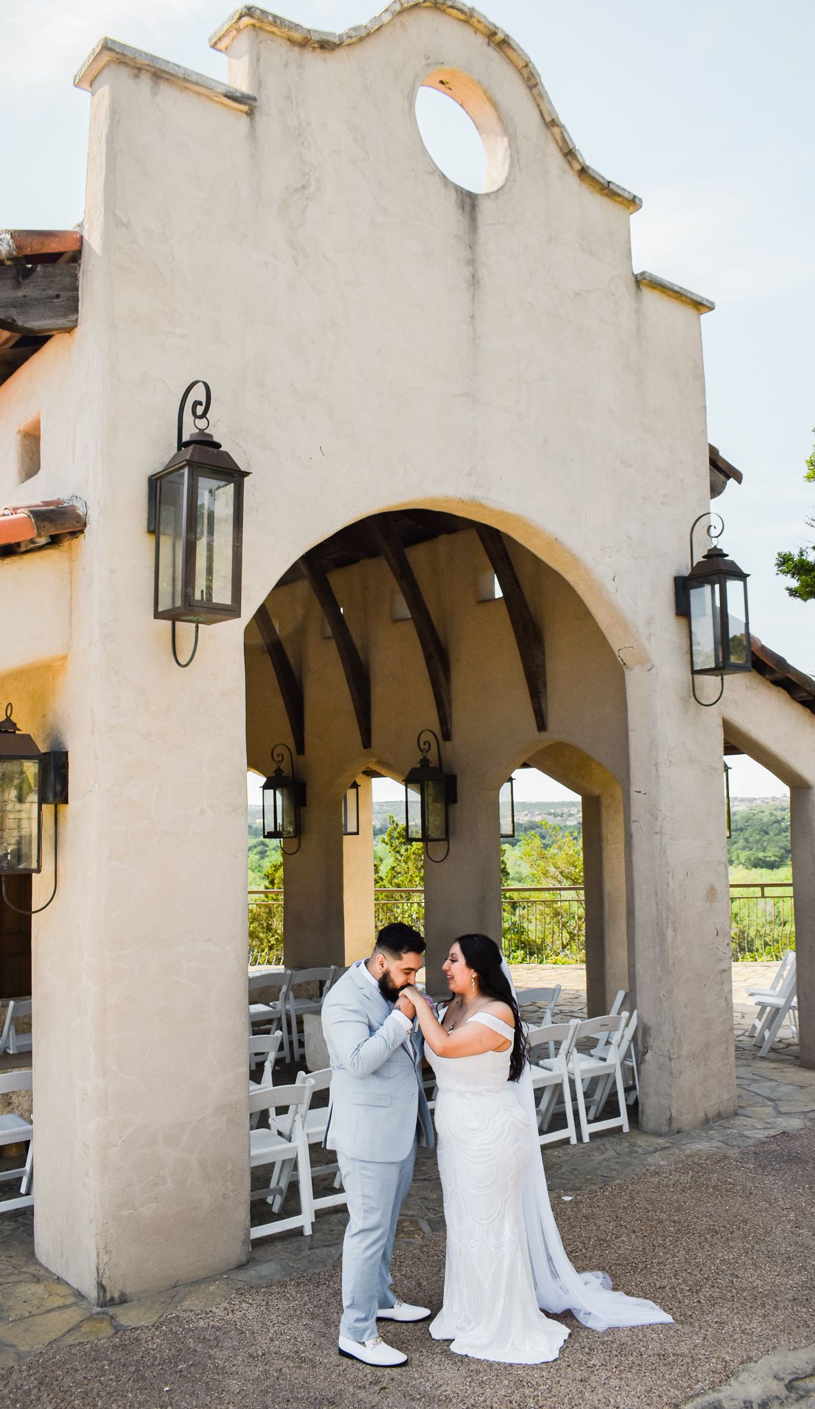 Newlyweds in light blue suit and white dress embracing under Spanish-style architecture.