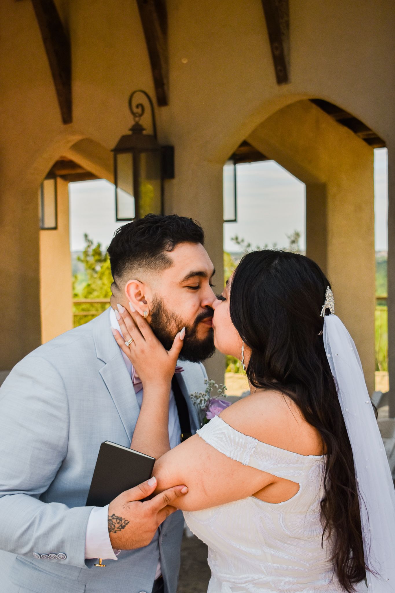 Intimate wedding moment captured under arched colonnade with hanging lanterns.