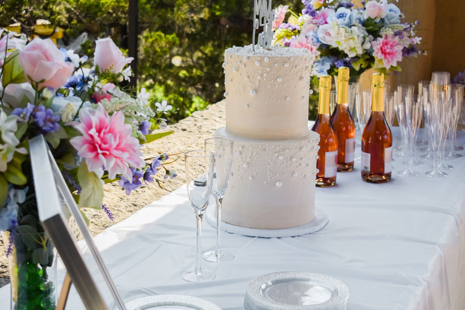 Elegant two-tiered white wedding cake with floral decorations and champagne bottles on a decorated reception table.