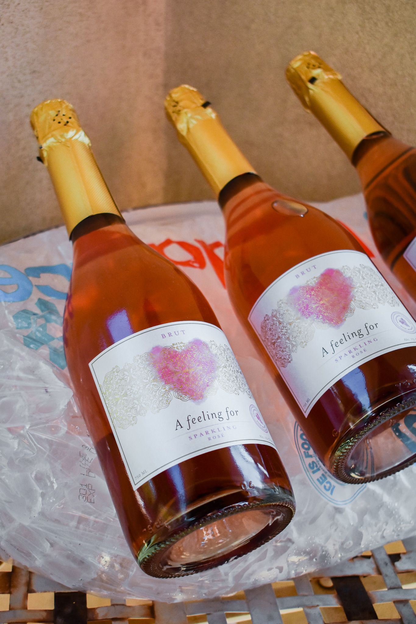 Three bottles of rose champagne with pink heart labels chilling in ice.