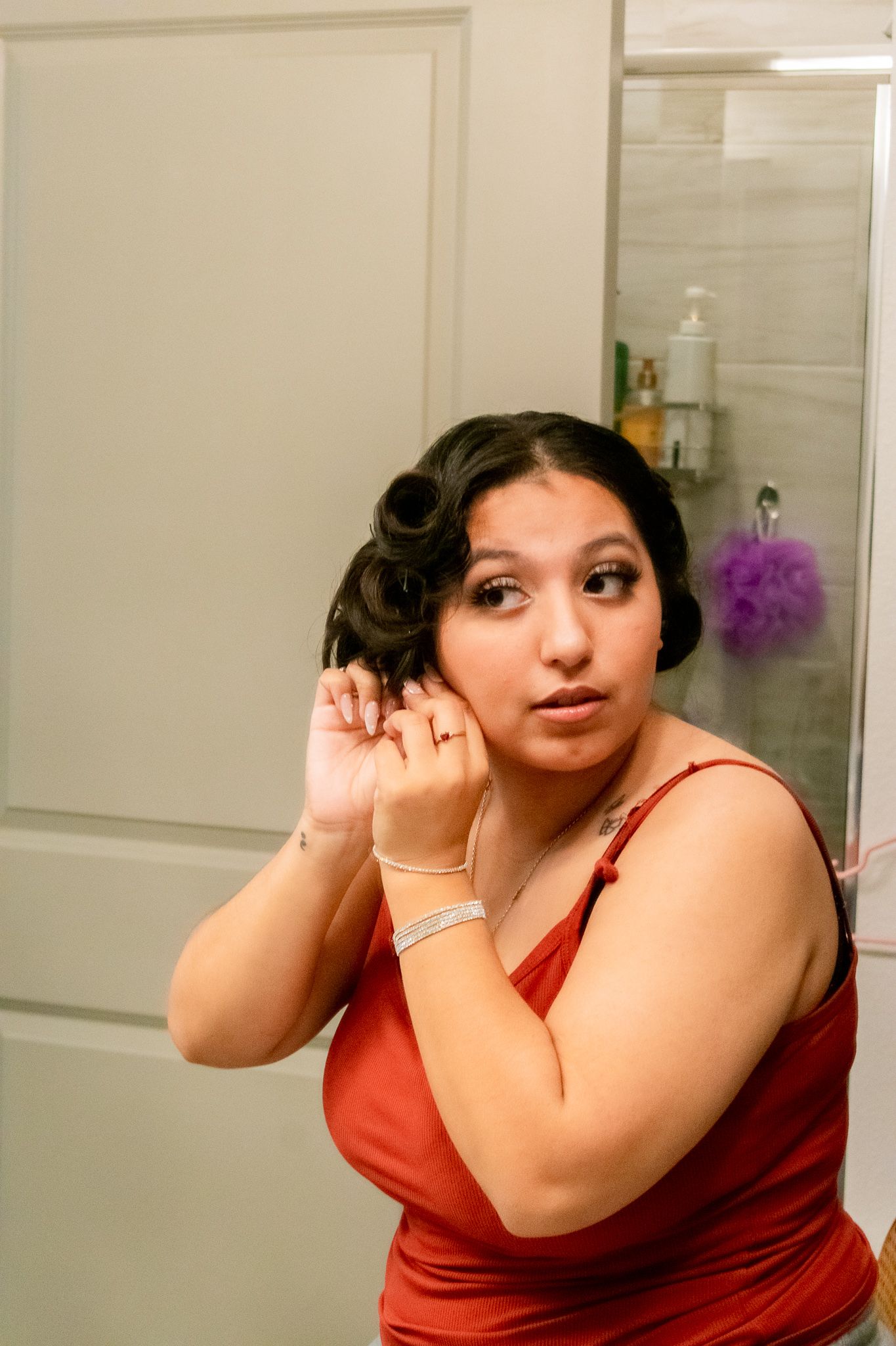 Woman with dark curled hair and red top showing off ring in bathroom mirror.