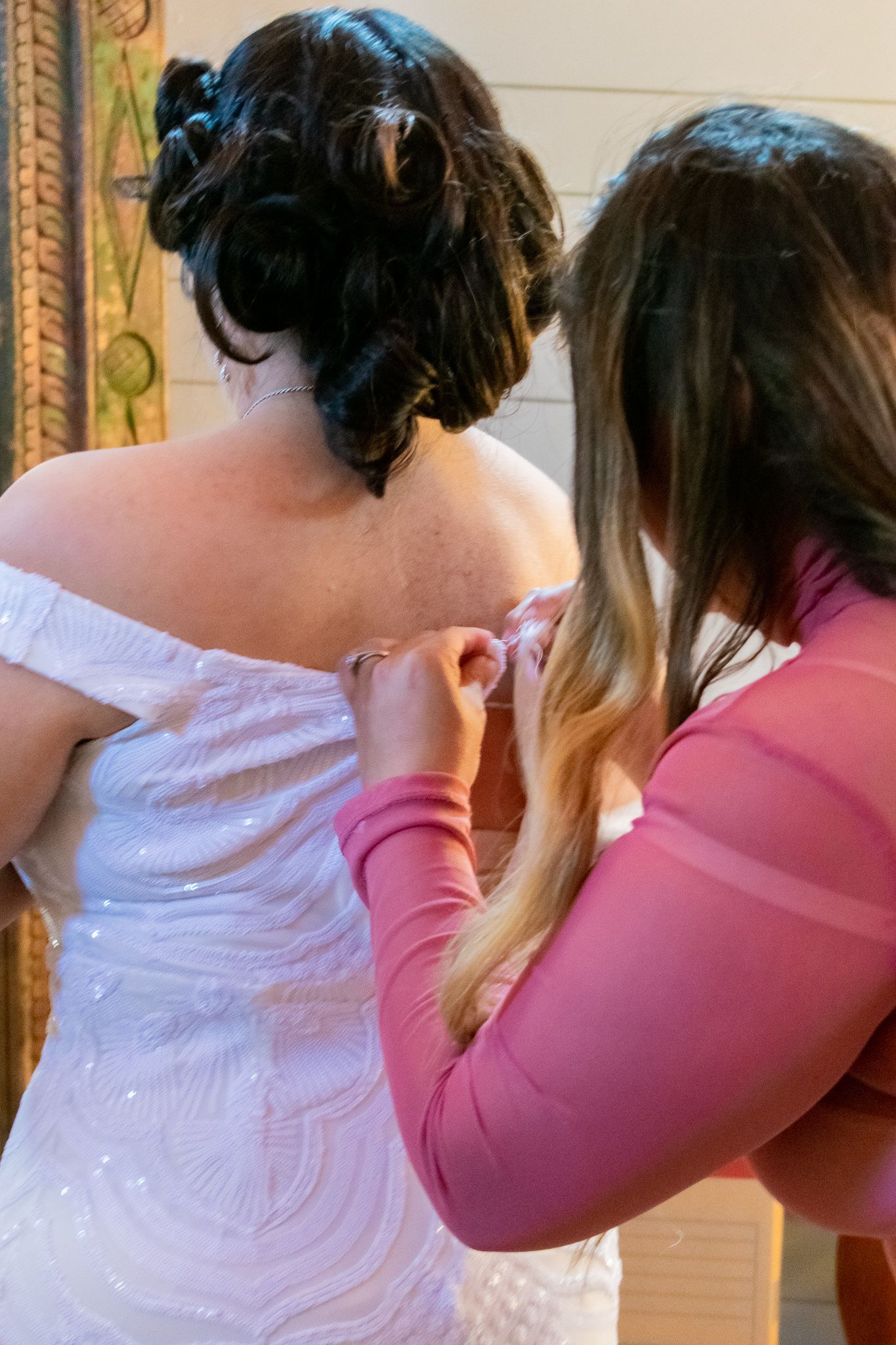 Wedding dress being buttoned up by someone wearing a pink top.