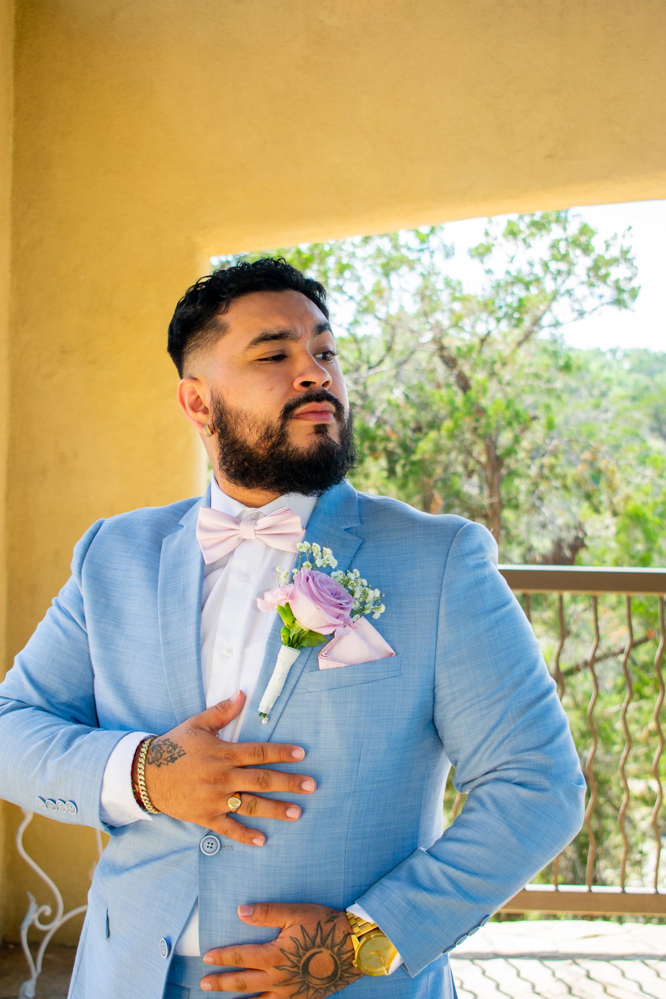Groom in powder blue suit with pink bowtie poses on balcony.