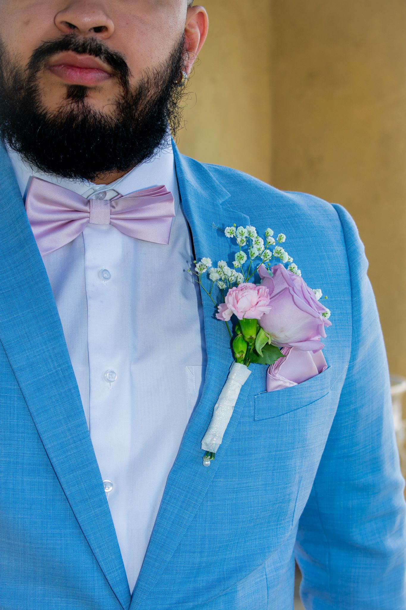 Close up of light blue suit jacket with purple rose boutonniere and pink bow tie.