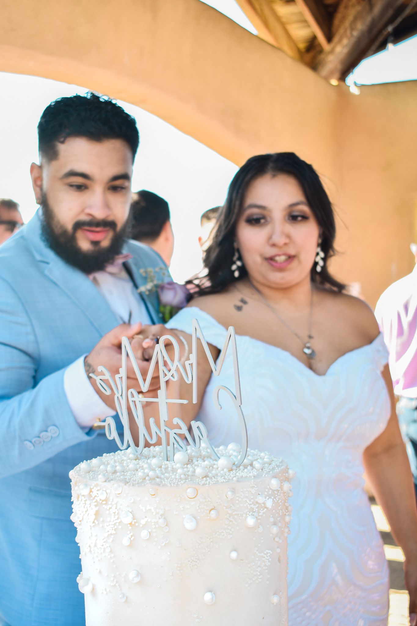 A couple stands together at their wedding reception, admiring their decorated white cake.