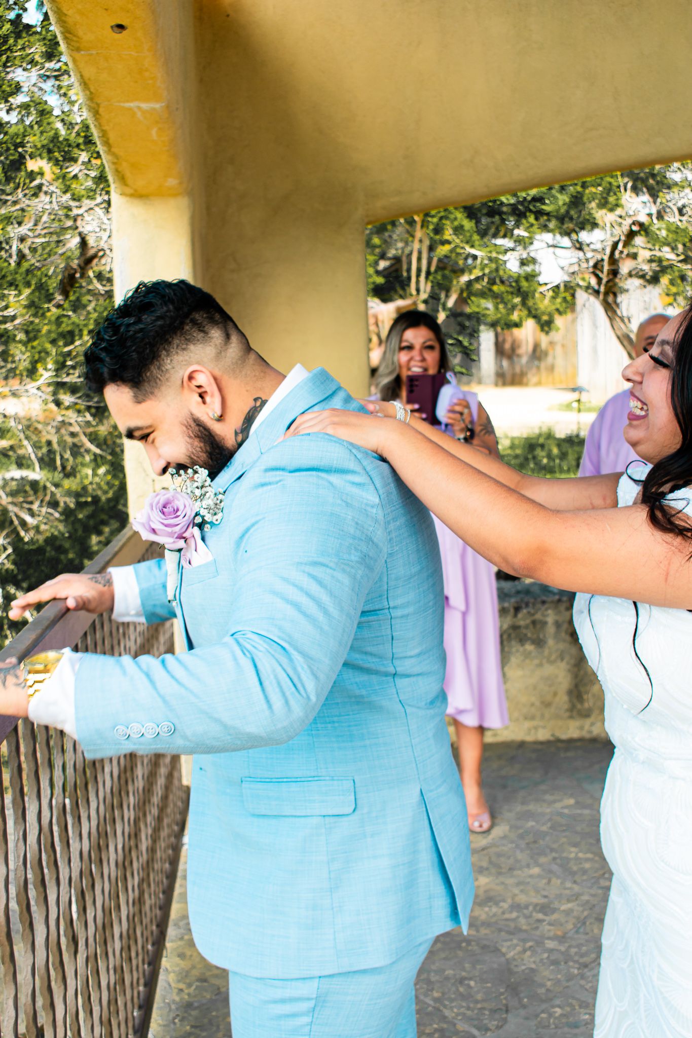 A couple sharing a playful moment at their wedding, with the bride in white and groom in light blue.