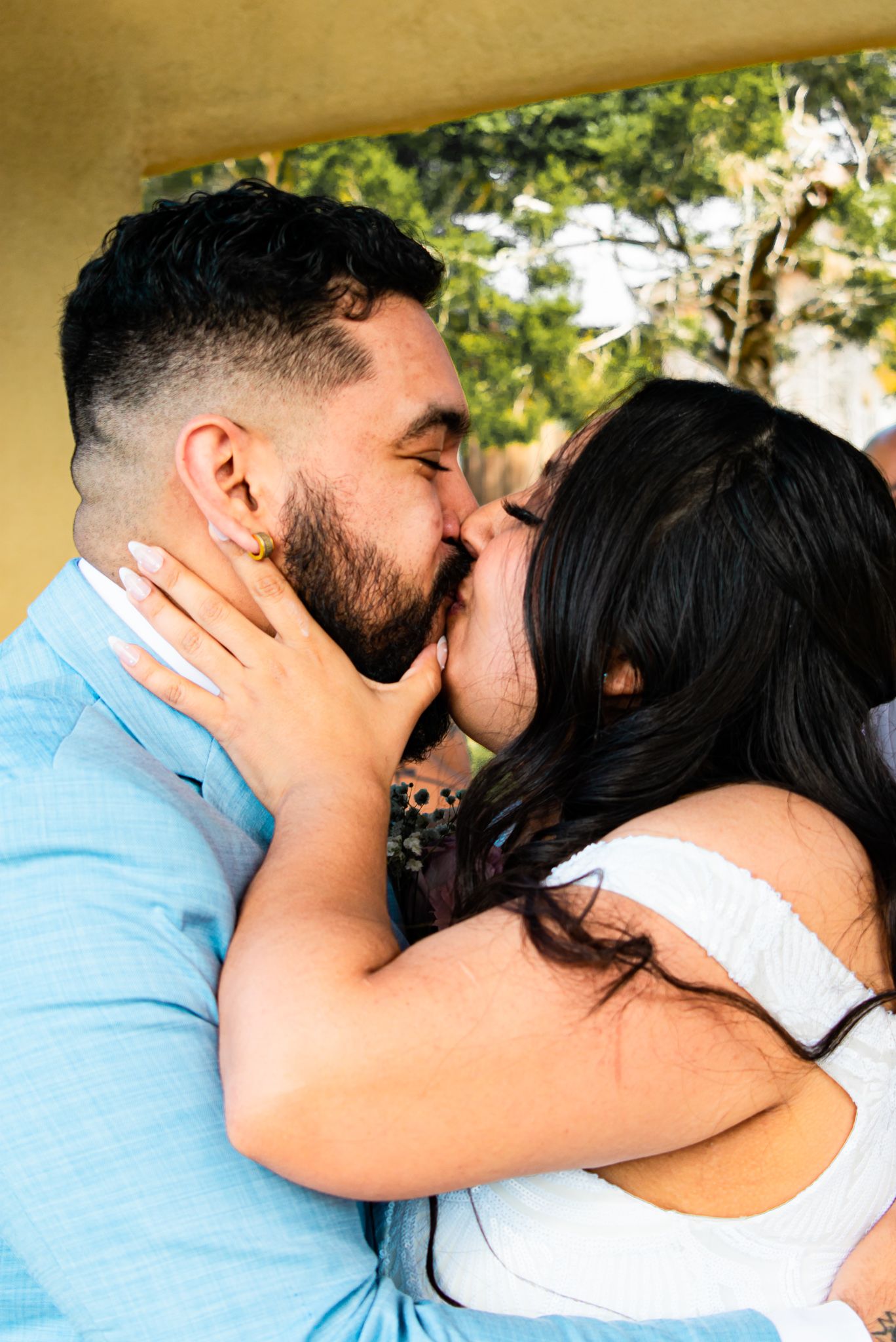A romantic couple embracing and kissing under a covered outdoor area.