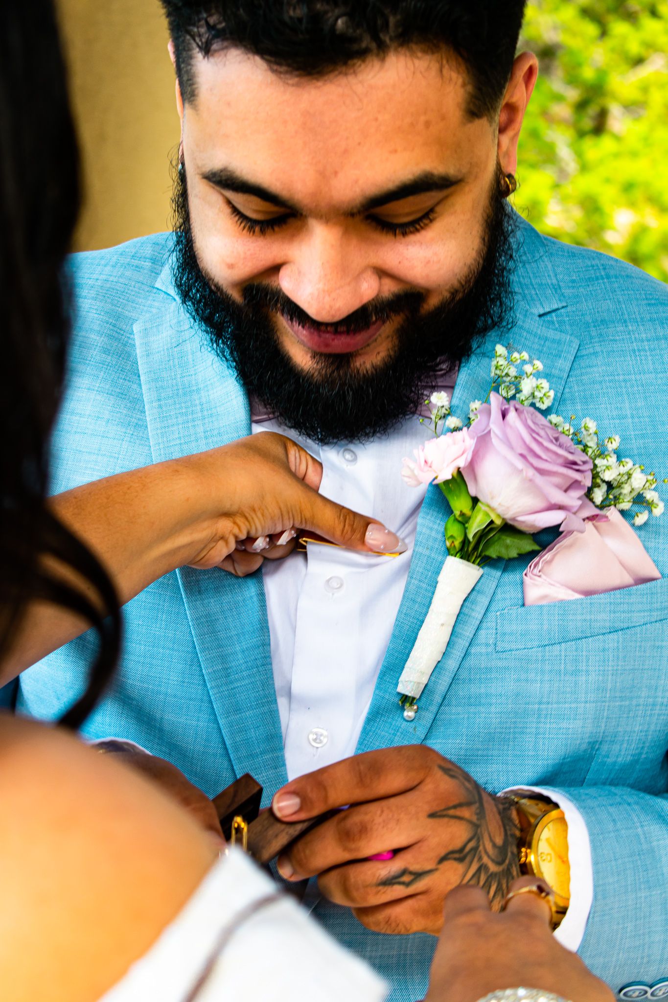 A close-up of hands adjusting a pink rose boutonniere on a light blue suit jacket.