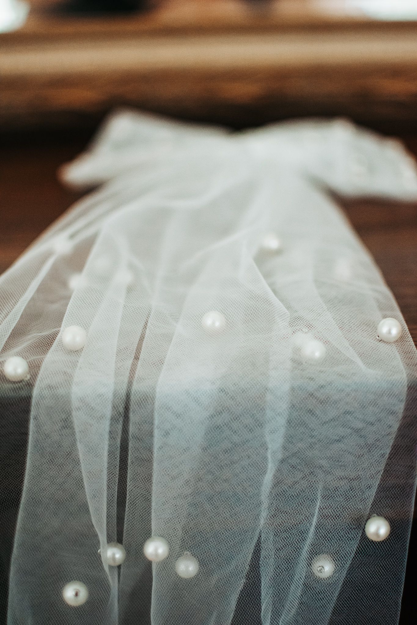 Delicate white bridal veil with scattered pearl details against a dark wooden surface.