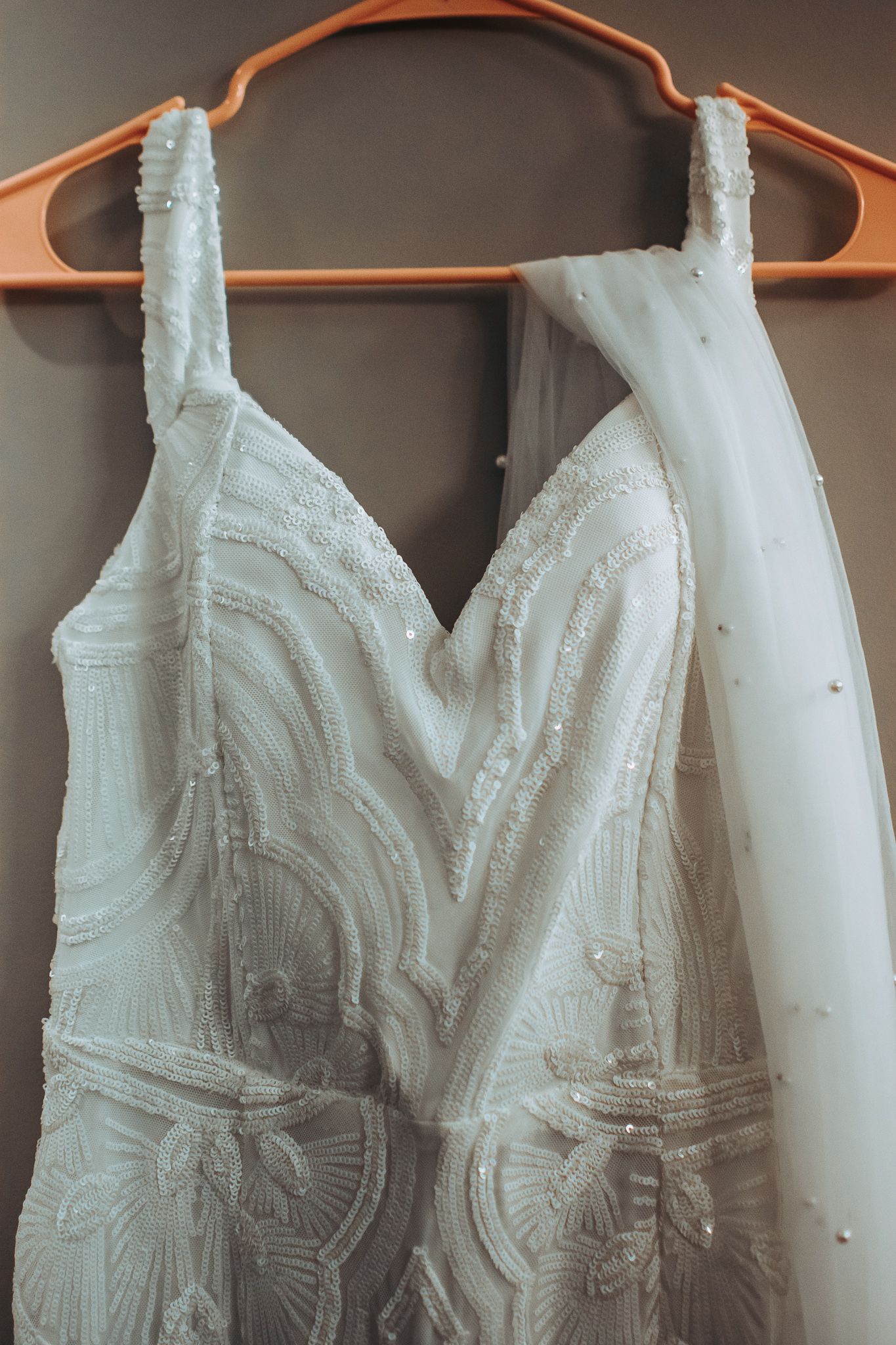 White wedding dress with intricate lace detailing hanging on an orange hanger.