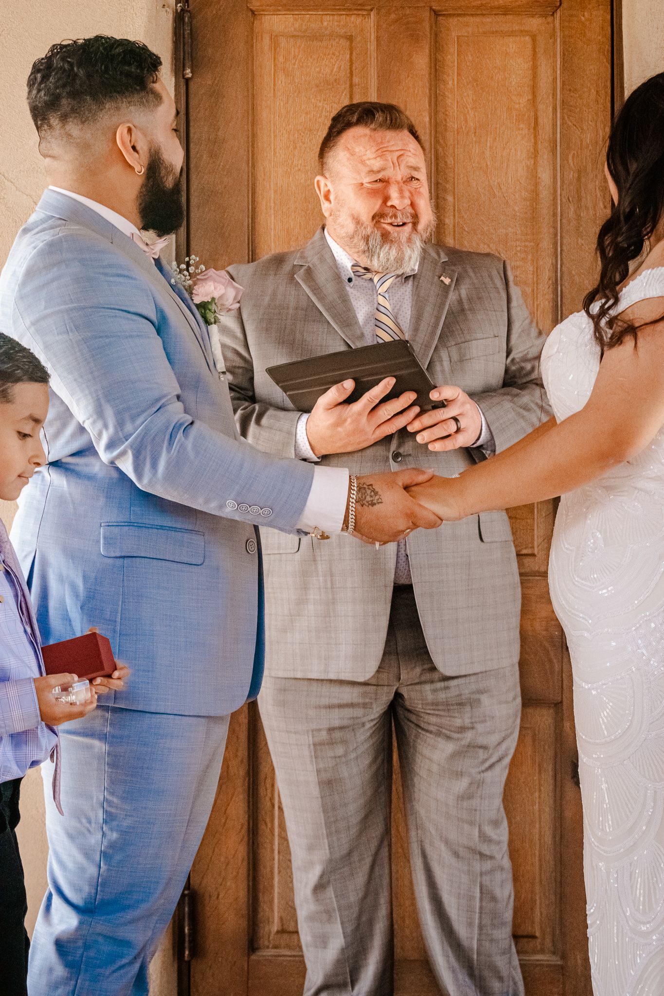 An intimate wedding ceremony with couple exchanging vows in front of an officiant in a grey suit.
