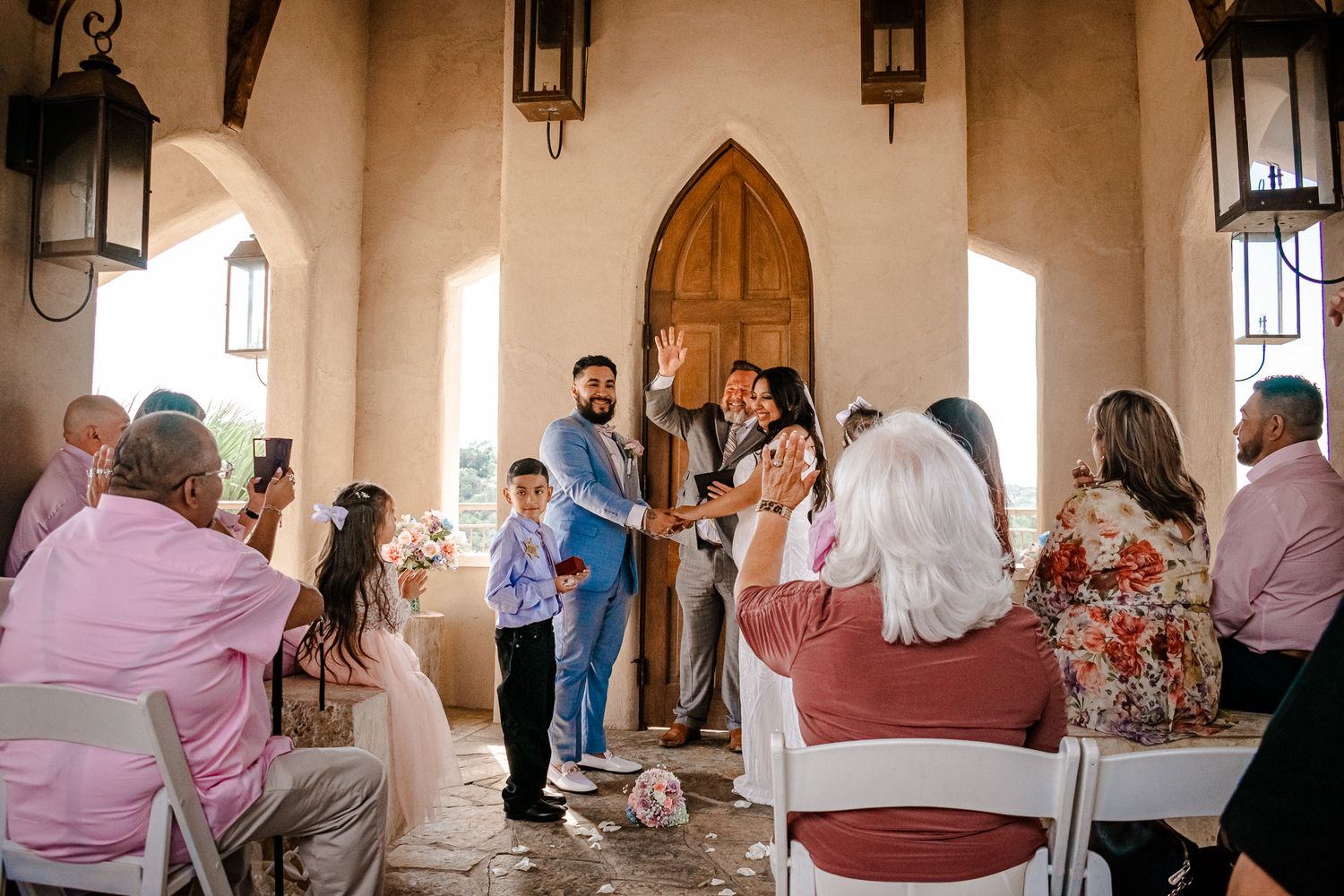 Wedding ceremony in a rustic chapel with arched doorways and hanging lanterns.