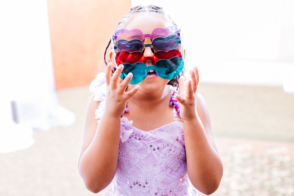 Young child wearing multiple pairs of novelty sunglasses stacked on their face.